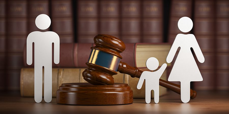 White paper-cutout figures of a man, a woman, and a child standing around a wooden gavel in front of a shelf of law books