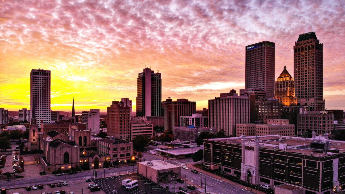 Downtown Tulsa skyline at sunrise, with office towers and a church spire under a pink and orange sky