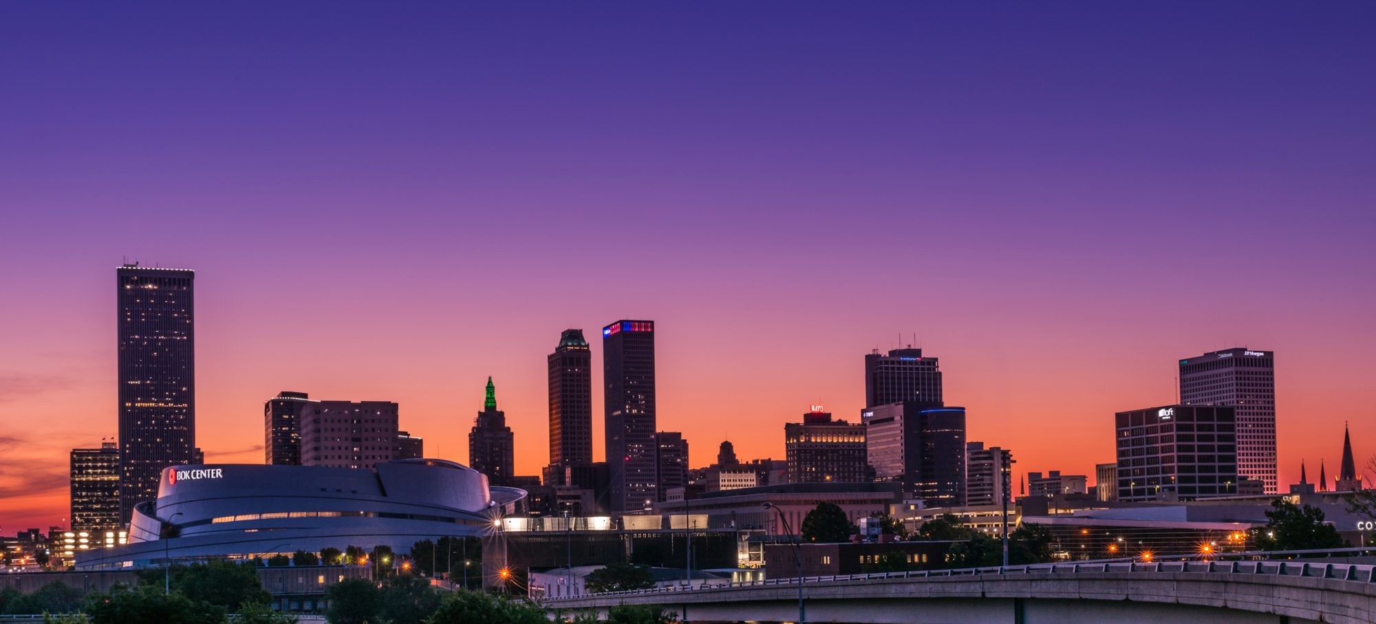 Downtown Tulsa skyline at dusk, with the BOK Center and office towers under a violet and orange sky